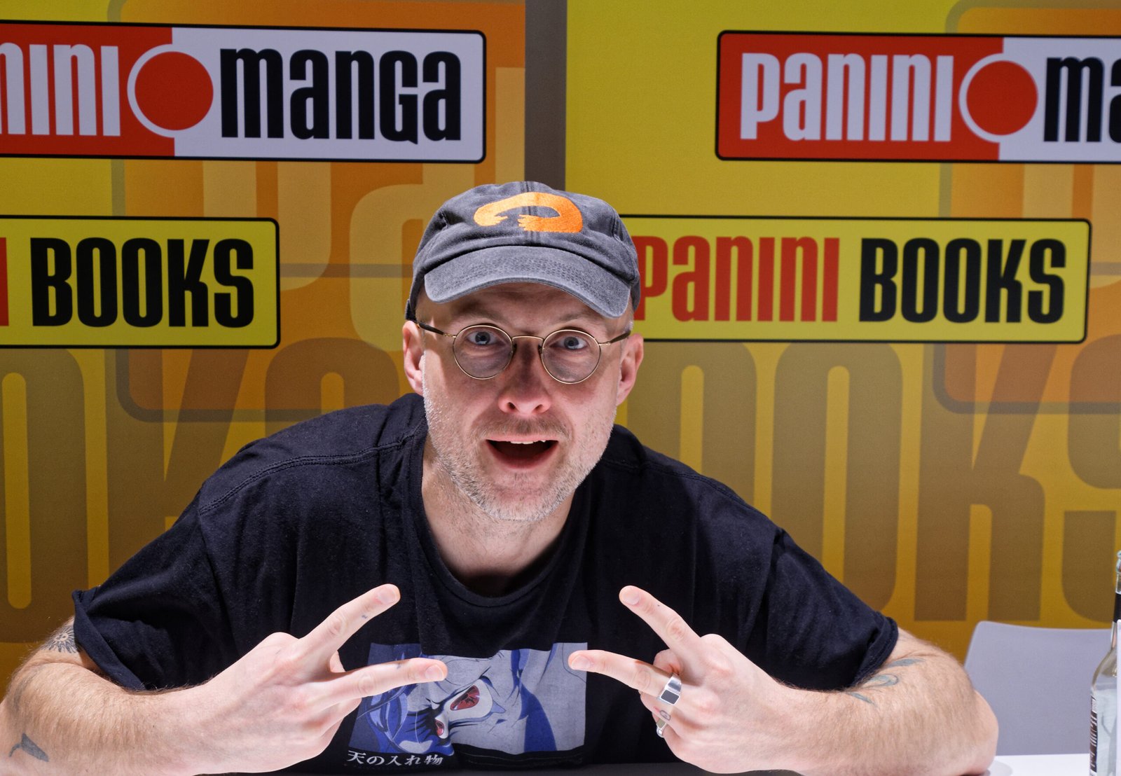 Bartosz Sztybor con gorra y lentes, sentado frente a un fondo de Panini en Comic Con Stuttgart 2025.