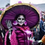 Participante con maquillaje de catrina y sombrero morado en la procesión de 2019.