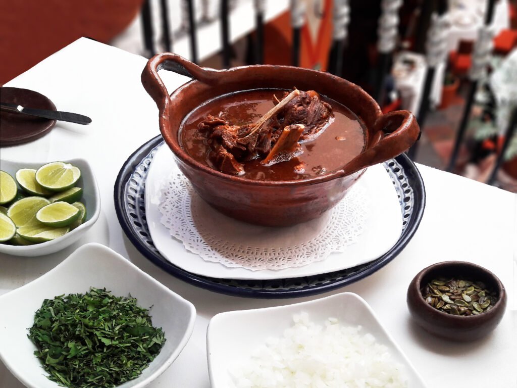 Huaxmole de caderas servido en cazuela, acompañado por limón, cebolla, hierbas y semillas de guaje; fotografía de archivo de 2017.