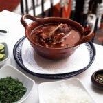Huaxmole de caderas servido en cazuela, acompañado por limón, cebolla, hierbas y semillas de guaje; fotografía de archivo de 2017.